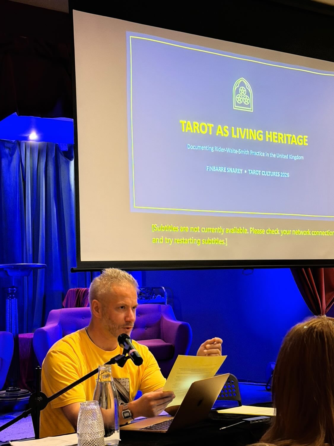 Finbarre Snarey speaking at Tarot Cultures 2026 on “Tarot as Living Heritage,” a presentation about Rider-Waite-Smith tarot practice in the United Kingdom, Living Heritage, tarot research and the British Tarot Archive.