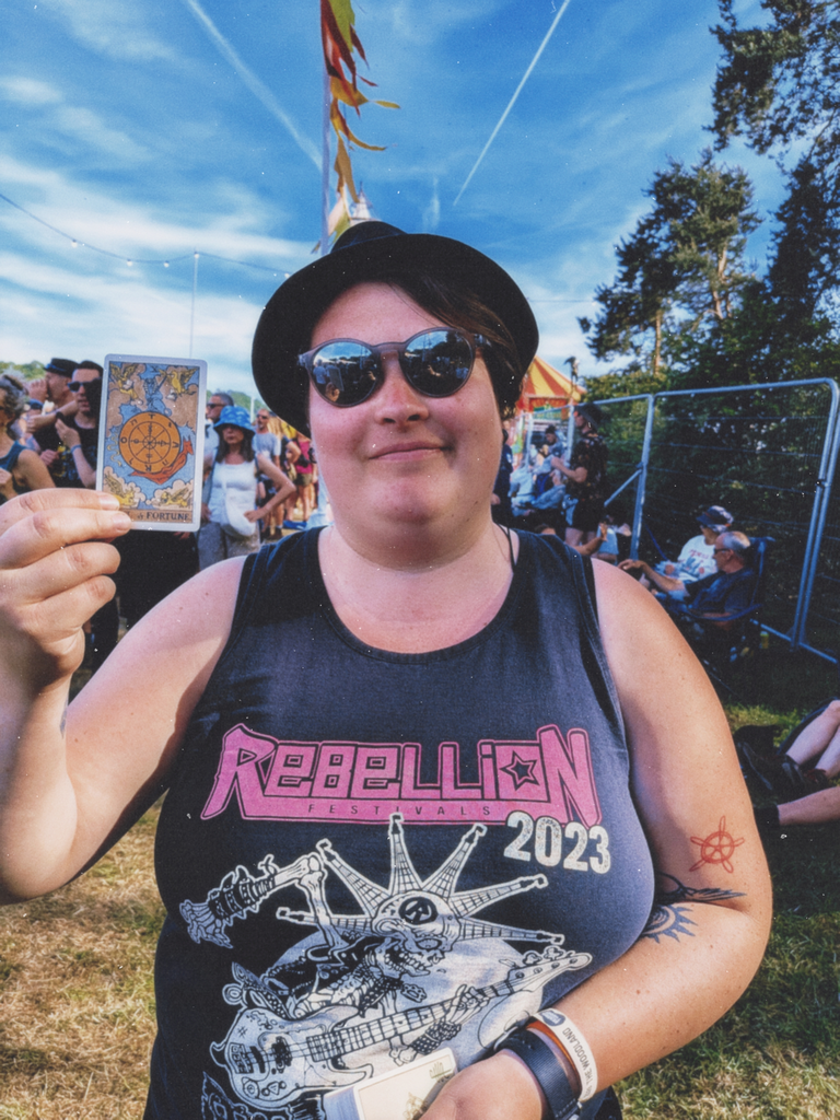 Festival-goer in a black Rebellion Festivals vest holding the Wheel of Fortune tarot card.