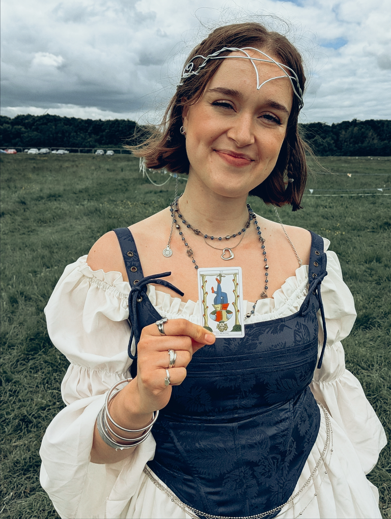 Festival-goer in a blue and white medieval-style dress holding The Hanged Man tarot card.