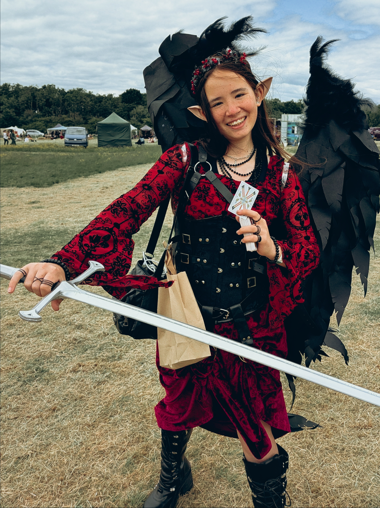 Smiling fantasy-costumed festival-goer with black wings, pointed ears, a sword and tarot cards.