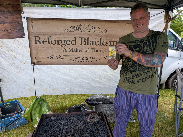 Blacksmith trader standing beside a Reforged Blacksmith sign while holding a tarot card.