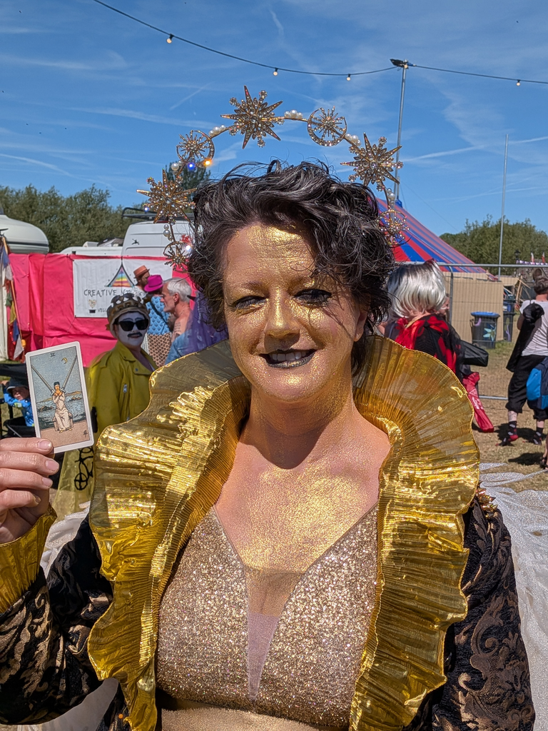 Gold-painted festival performer in a celestial costume holding the Two of Swords tarot card.