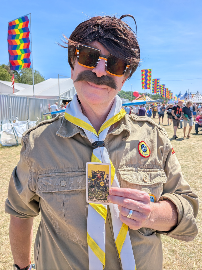 Festival-goer dressed as a scout leader holding the King of Pentacles tarot card at Bearded Theory.