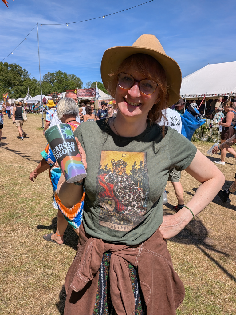 Smiling festival-goer wearing a tarot-themed Empress T-shirt and holding a Bearded Theory cup.