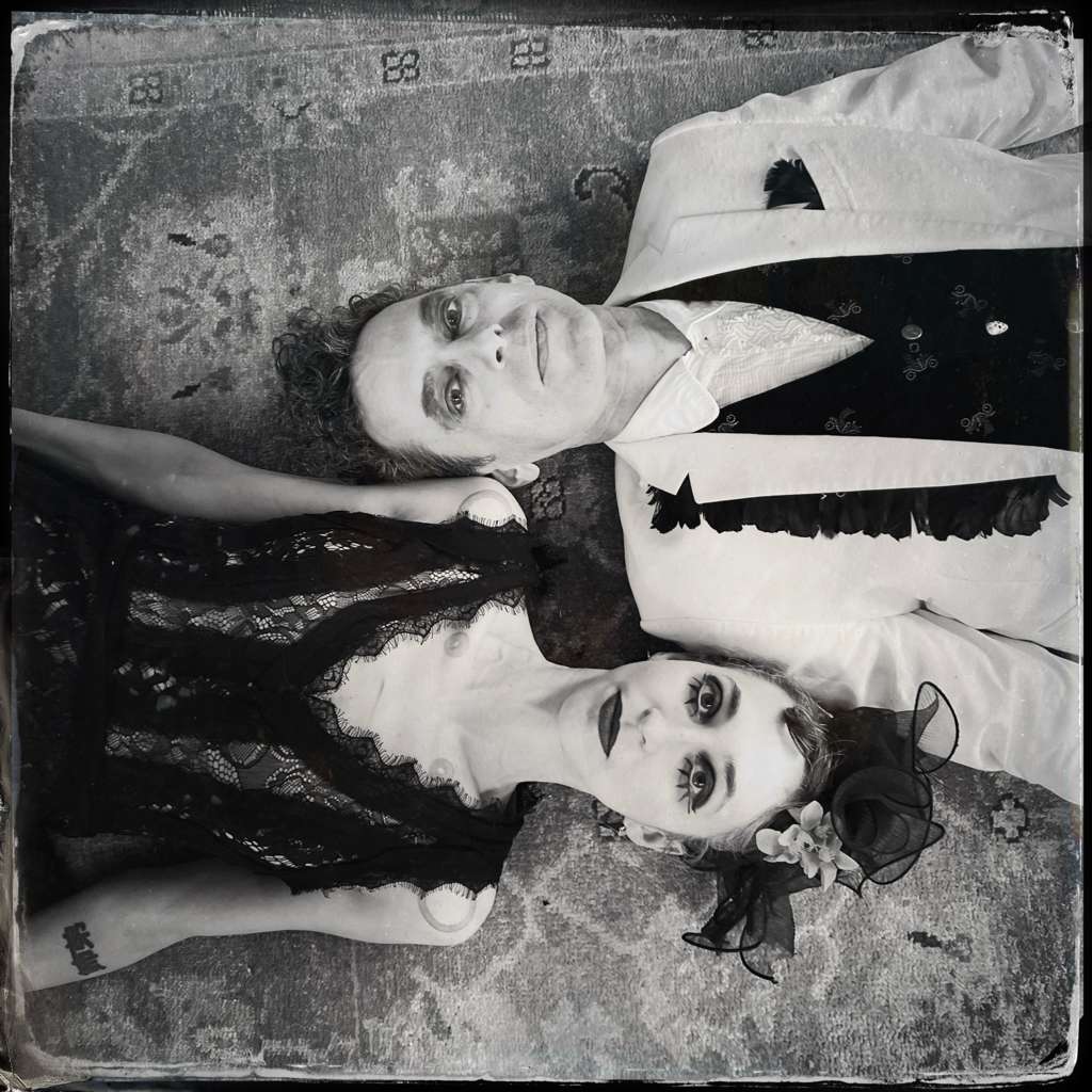 Black-and-white promotional portrait of the two members of Charming Disaster lying side by side in theatrical gothic clothing.