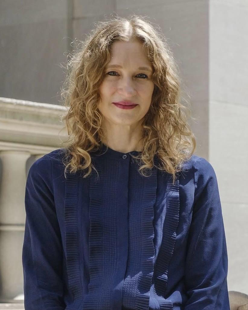 Portrait of Claire Gilman, Acquavella Curator at the Morgan Library & Museum, wearing a navy blouse against a pale stone background.